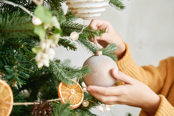 A light Christmas bauble with a powder imitating frost in the hands of a girl who hangs it on the Christmas tree