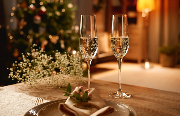A couple of glasses of champagne are on a Christmas table with a serving decorated with flowers in a room with a festive magical atmosphere