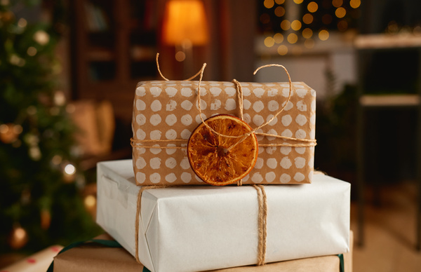 A Christmas gift box in a craft package with an ornament decorated with a dried slice of orange stands on a larger white box with twine