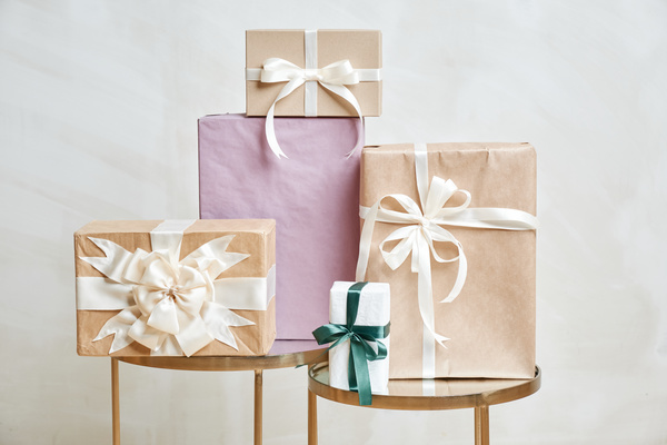 Gift boxes wrapped in light paper and decorated with ribbons on metal racks on a white background
