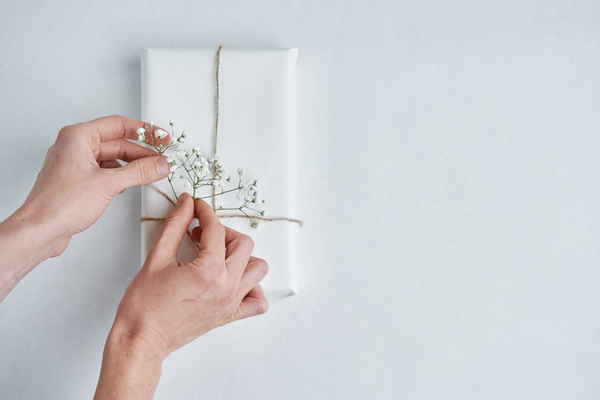 A gift wrapped in light paper and tied with twine being decorated with a sprig of white gypsophyila