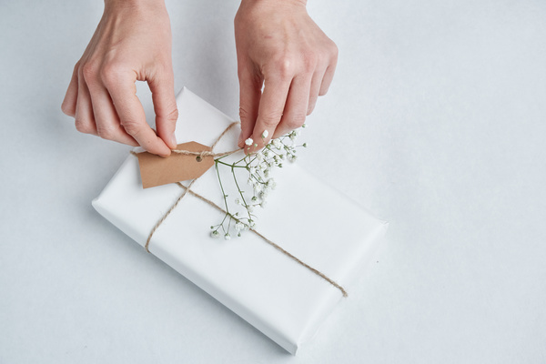 A twine being tied on a gift with a tag in white wrapping paper decorated with a gypsophila