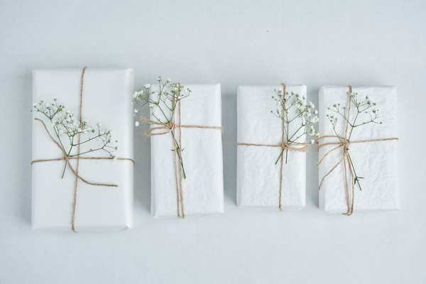 Presents wrapped in white paper tied with twine and decorated with flowers are in a row on a light surface