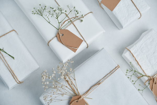 Sequential flatlay of gifts in white packaging tied with thin ropes with tags on them and decorated with white gypsophiles