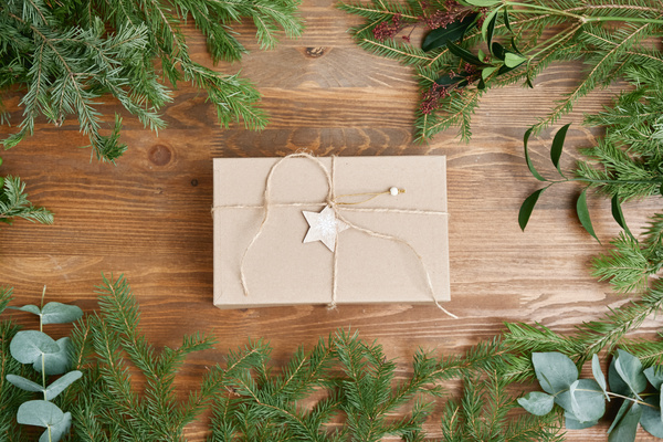 A craft gift box tied with twine with a star on it on the table in the middle of Christmas tree branches and various plants