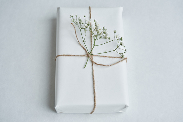 A gift wrapped in white paper tied with string and decorated with a flower on a white background