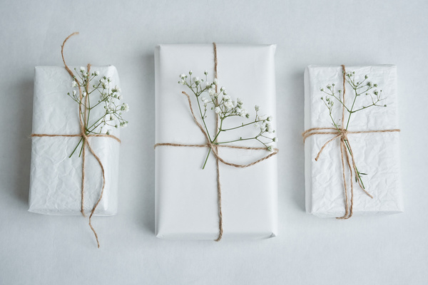 Gifts packed in white paper tied with string and decorated with flowers on a light background