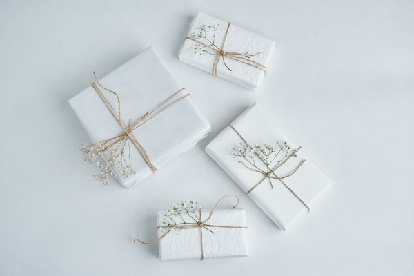 Present wrapped in white paper tied with twine and decorated with flowers are laid out on a light surface