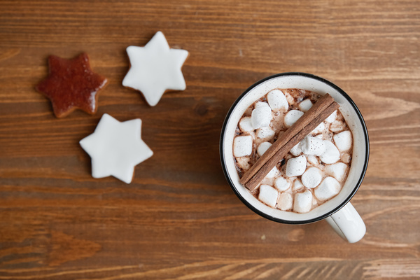 Cocoa with cinnamon and marshmallows in a white mug with a black border with glazed gingerbread stars on a wooden table