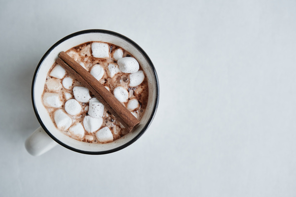 Cocoa with cinnamon stick and marshmallows in a light mug with a black border on a white surface