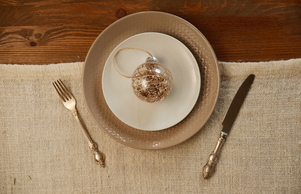 A glass Christmas bauble with sequins on a dish served for Christmas dinner on a table with cutlery and a rag napkin