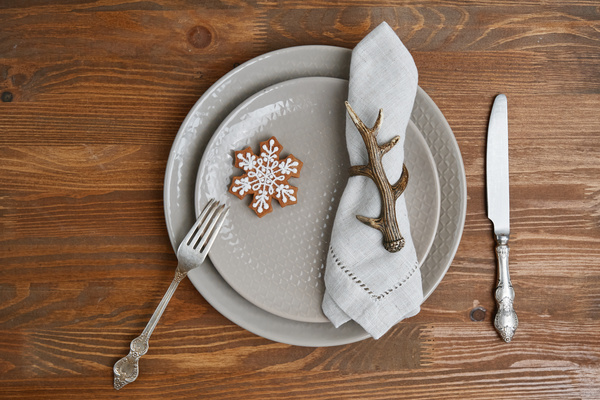 Serving a platter for Christmas dinner with a gingerbread snowflake and a napkin decorated with a metal ring in the form of a branch on a platter next to silverware