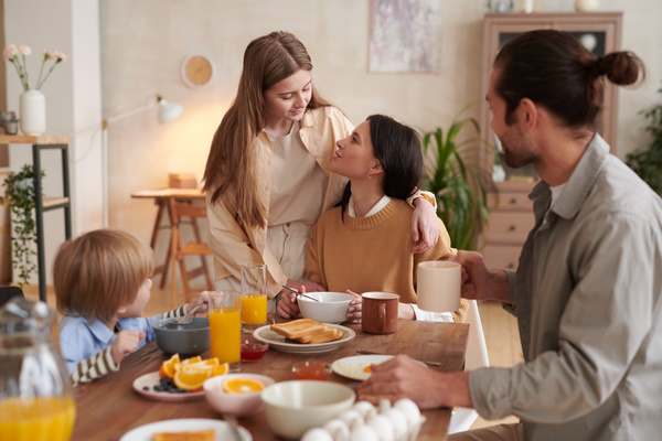 A girl communicates with her mother sitting at the table with her husband and young son at a family breakfast