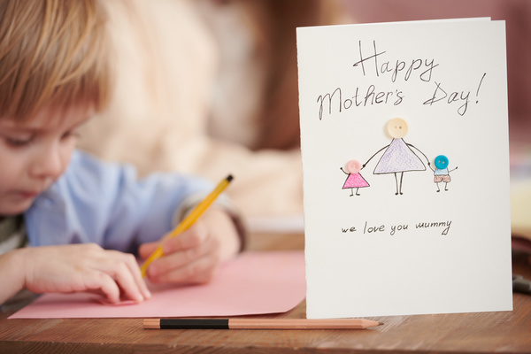Close-up of a handmade postcard in honor of Mothers Day with a drawing inscription and applique of small buttons standing on the table next to a pencil
