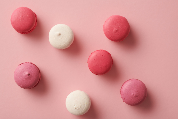 Top view of pink and white macaroons spread out on a pink surface