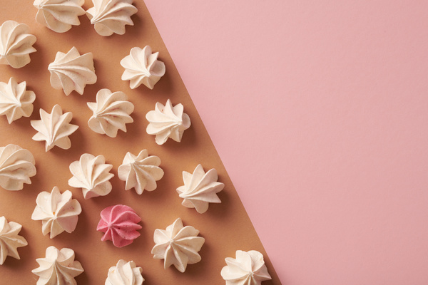 A pink meringue is surrounded by white ones lying on a surface divided into brown and pink parts