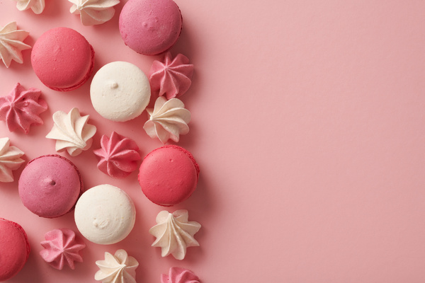 Top view of pink and white macaroons and meringues lying on one half of the pink surface