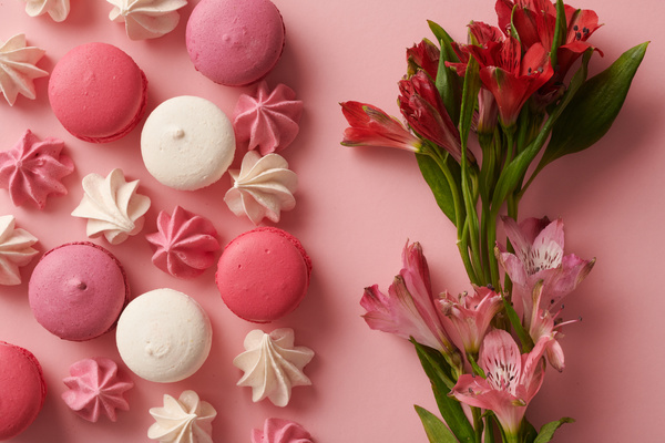 Pink and white meringues and macaroons with bright lilies are on a pink surface