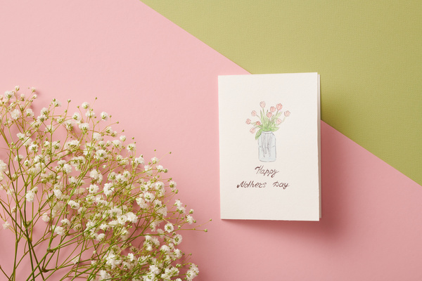 A homemade Mothers Day card with an illustration and a sprig of white gypsophiles on a two-tone background