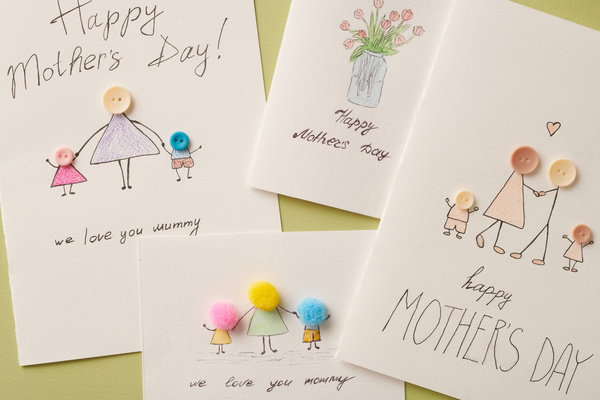 Top view of homemade postcards for Mothers Day with thematic illustrations and applications on a green background