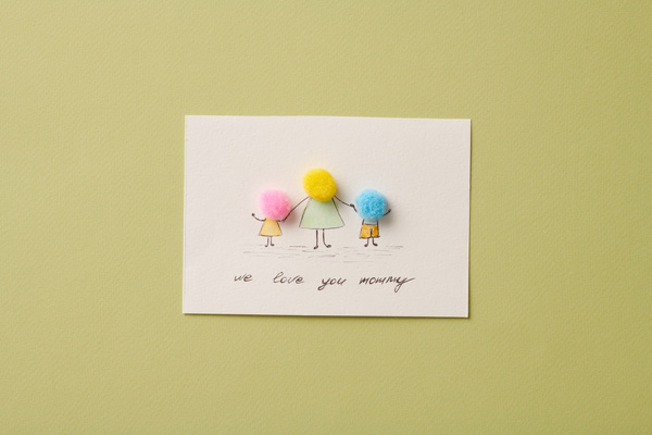 Handmade postcard in honor of Mothers Day with a thematic picture and pompoms lying on a bright green background
