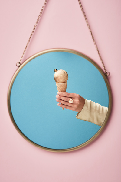 Reflection in a round mirror hanging on a gold chain of a golden frosted Christmas ball with a crown fastener in a waffle cone reminiscent of ice cream which is held in the hand with a ring on the middle finger