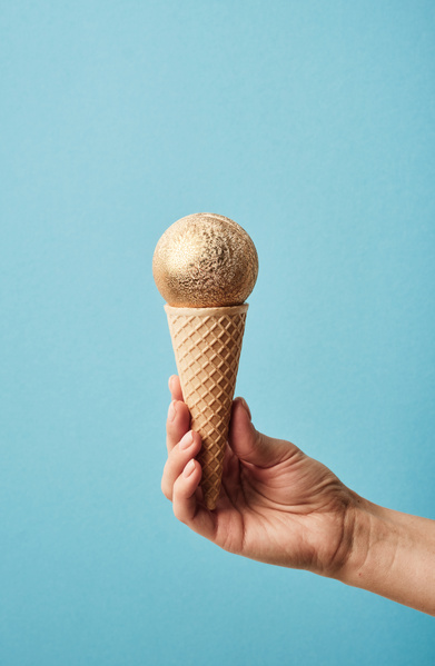A golden frosted Christmas ball which is in a waffle cone that is held on a blue background reminds of ice cream