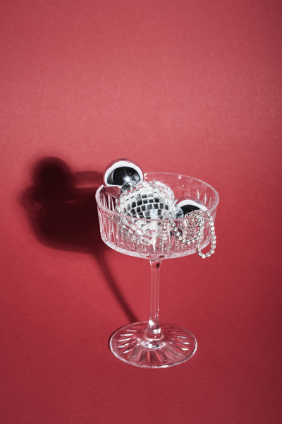 A crystal glass with silver Christmas decorations stands on a fuchsia background