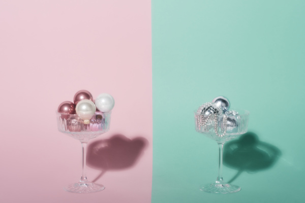 Blurred image of champagne glasses filled with pink white and silver Christmas balls standing on blue and pink backgrounds