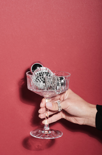 Champagne glass with silver Christmas decorations in a womans hand with a ring on a fuchsia background