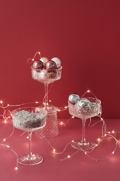A champagne glass with rhinestones stands next to other glasses with Christmas balls twined with a garland