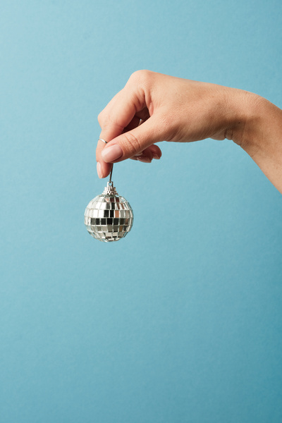 A man holds a Christmas tree toy in the form of a small disco ball on a blue background by a silver lace
