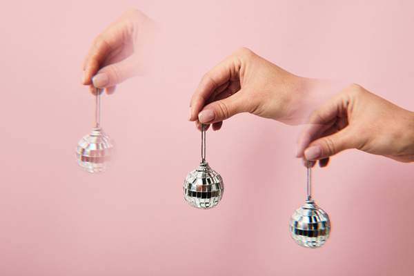 Duplicate images of a small disco ball held by a silver lace on a pink background