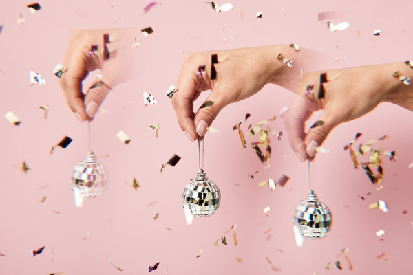 Repeated images of a small disco ball held by a silver cord with falling golden confetti on a pink background