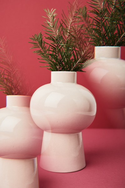A repeating image of a Christmas tree branch in a white spherical vase on a high leg on a fuchsia background