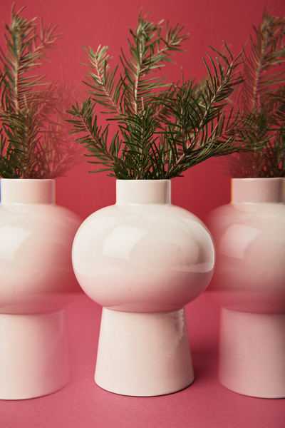 Duplicated image of a fresh Christmas tree branch in a white vase of unusual shape on a high leg on a fuchsia background