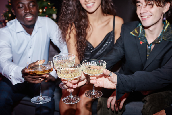 Elegantly dressed people are sitting and clinking wide carved glasses full of champagne celebrating the new year