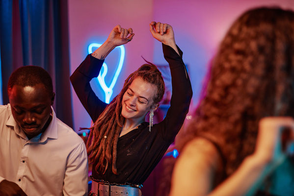 A woman with dreadlocks and long earrings dressed in a black blouse rejoicing and dancing celebrates the New year with friends