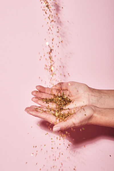 Golden confetti in the shape of stars pours into womens palms on a pink background