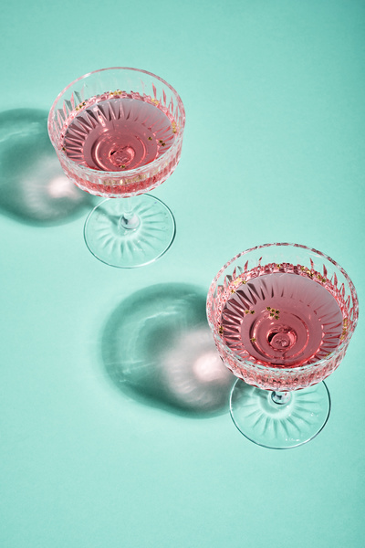 Two wide crystal glasses filled with pink wine and golden stars casting shadows on the blue surface