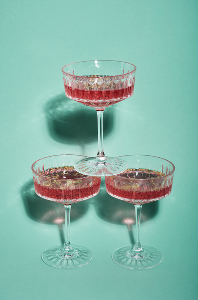 On two identical wide glasses with high legs filled with pink wine and golden stars stands one more on a blue background