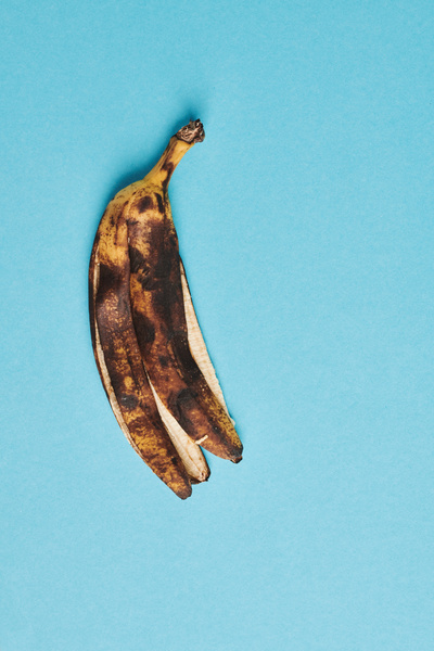 A ripe banana in dark spots is with its stem up on a blue surface