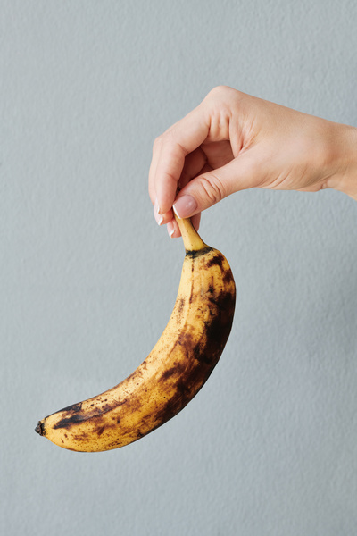 Ripe banana with dark spots in the female hand against a white background