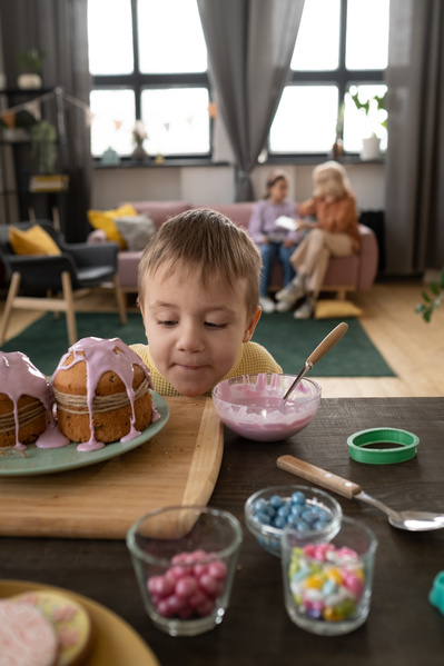 A blond boy in a yellow sweater and Easter cakes decorated with twine and pink icing on the table