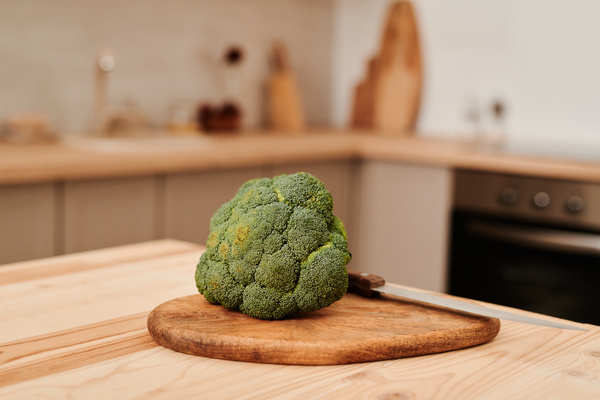 Fresh broccoli inflorescences on a cutting wooden board with a knife in a bright kitchen