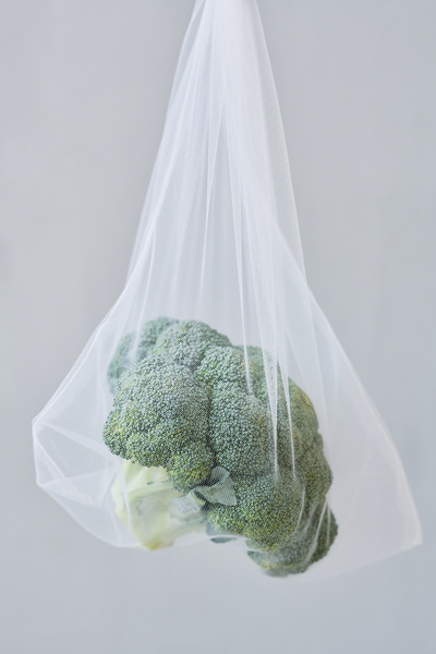 Fresh broccoli in a white eco-mesh bag suspended on a green string against a light background