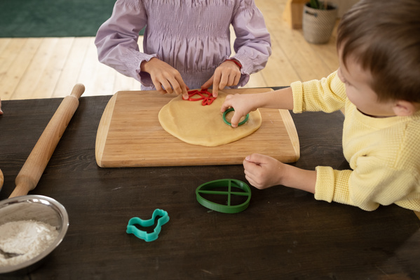 Brother and sister cutting out cookies from dough on a wooden cutting board with colorful plastic molds