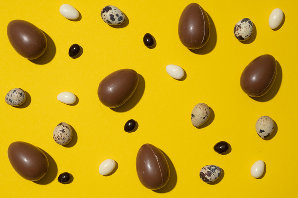 Chocolate and quail eggs are scattered on a yellow surface with balls of dark and white chocolate