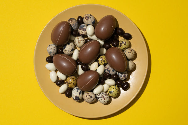 Chocolate and quail eggs with balls of dark and white chocolate on a plate which is on a yellow surface