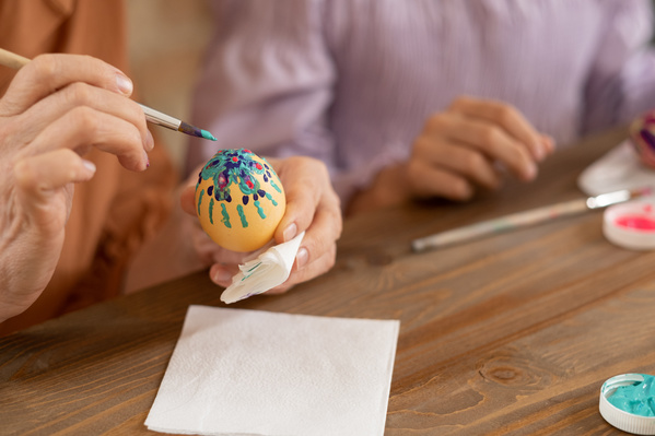 A Chicken Easter egg decorated with a flower pattern in the hand and a brush in turquoise paint